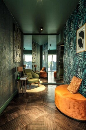 A modern living room with a green sofa, a green armchair, and a wooden coffee table. There are abstract wall art pieces and a large window in the background. - Liv Urban Larnaca (Larnaca)