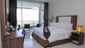 Ein Hotelzimmer mit einem großen Bett, einem Schreibtisch, einem Sessel, einem Balkon mit Tisch und Stühlen sowie einem Nachttisch mit Lampe.