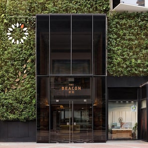 Fachada moderna de un edificio con entrada de vidrio, un letrero que dice 'The Beacon' y un jardín vertical a la izquierda.