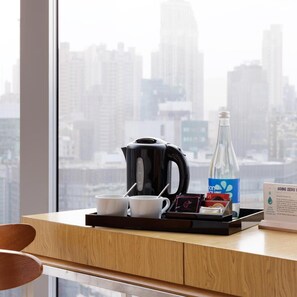 Habitación de hotel con vista a la ciudad, cafetera, dos tazas, botella de agua y bandeja con un cartel sobre reducir residuos.
