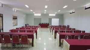 Un salón de conferencias con filas de mesas y sillas, una pantalla de proyector y un atril.