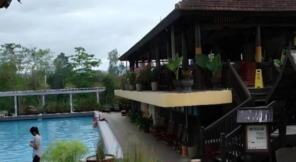 Un área de piscina con terraza de madera, plantas en macetas y una zona de estar cubierta.