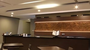 Un espace d’accueil moderne, doté d’un comptoir de réception en bois, d’un éclairage au plafond et d’un coin salon avec des tables et des chaises.