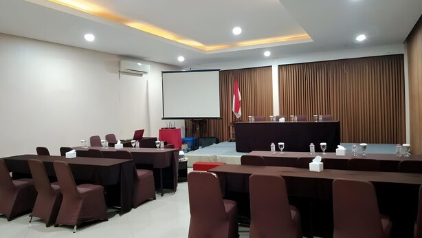 Une salle de conférence équipée de tables, de chaises, d’un pupitre, d’un écran de projection et d’un drapeau.
