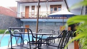 A pool area with chairs and a table, a building with a balcony, and a clear view of the water. - The Priangan Boutique Hotel (Ciamis)