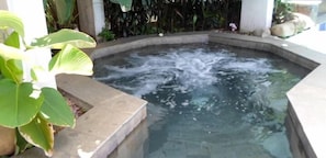 A hot spring with water bubbling, surrounded by a concrete edge and greenery.