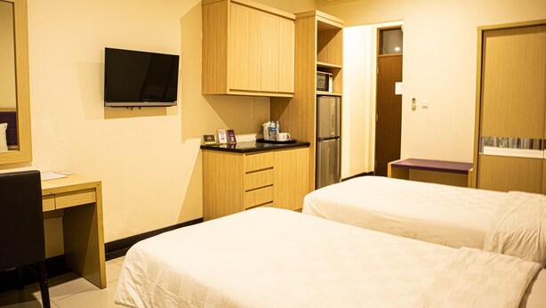 A hotel room with two beds, a desk, a TV, a kitchenette with a fridge and microwave, and an air conditioning unit. - Rukun Resort Sentul (Citaringgul)