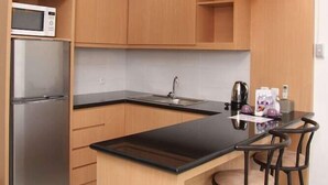 A modern kitchen with wooden cabinets, a stainless steel refrigerator, a black countertop, and a bar area with stools. - Rukun Resort Sentul (Citaringgul)