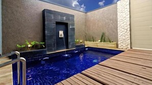 Ein Poolbereich mit Holzterrasse, Steinmauer und einer Tür zu einem überdachten Bereich.