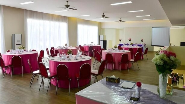 Ein Konferenzraum mit mehreren runden Tischen, roten Stühlen, Deckenventilatoren und einer Projektionsleinwand.