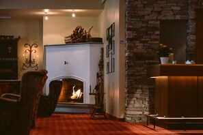 A cozy living room with a fireplace, a stone wall, and a wooden cabinet. - Hotel Union Geiranger (Stranda)