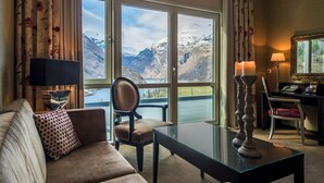 A cozy living room with a sofa, a chair, a glass coffee table, and a view of snow-capped mountains through large windows. - Hotel Union Geiranger (Stranda)