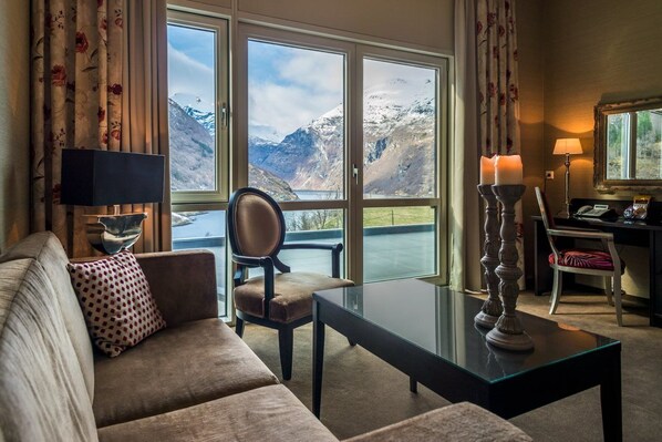A cozy living room with a sofa, a chair, a glass coffee table, and a view of snow-capped mountains through large windows. - Hotel Union Geiranger (Stranda)