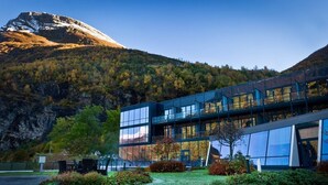 A modern building with large glass windows, surrounded by a well-maintained garden with various shrubs and a pathway leading to the entrance. - Hotel Union Geiranger (Stranda)