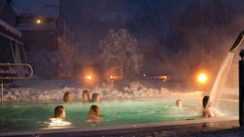 Zona de piscina exterior cubierta de nieve, con gente nadando y un jacuzzi a la derecha.