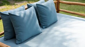 Una cama con almohadas azules y un cabecero de madera, ubicada en un jardín con plantas y un sendero de piedra.