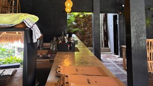 Zona de bar con techo de paja, lámparas colgantes y vistas a un jardín.