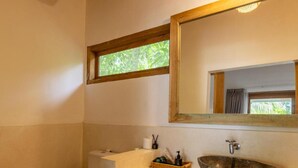 Un baño con inodoro blanco, un lavamanos de piedra, un espejo con marco de madera y una ventana con vistas a zonas verdes.