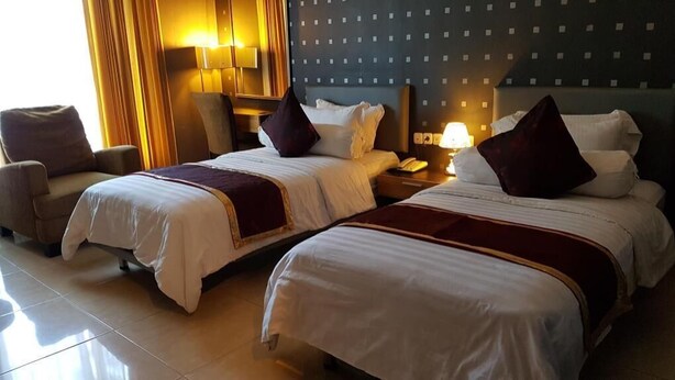 Une chambre d’hôtel avec deux lits, une chaise, une table de chevet avec une lampe et un mur orné d’un motif décoratif.