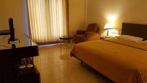 Une chambre d’hôtel avec un lit, un bureau, une chaise, une lampe et une fenêtre avec des rideaux.