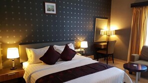 Una habitación de hotel con una cama, dos lámparas de noche, una silla, una mesita y un espejo.