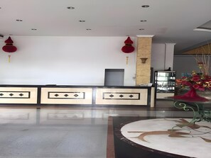 A reception area with a modern design, featuring a reception desk, a decorative vase with flowers, and a patterned floor. - Hotel Prima Indah (Sibolga)