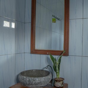 A bathroom with a stone sink, a wooden-framed mirror, and a potted plant. - Pakels Bali Villas (Karangasem)
