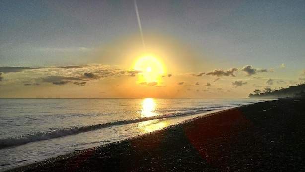 A beach with the sun setting over the ocean, creating a silhouette of the coastline. - Pakels Bali Villas (Karangasem)