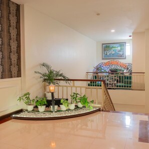 A hotel lobby with a staircase, potted plants, a decorative wall, and a painting. - Muara Hotel and Mall Ternate (Ternate)