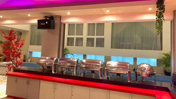 Zona de recepción de un hotel con mostrador, servicio de buffet y pantalla de televisión.