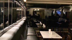 Un restaurante moderno con una barra larga, asientos acolchados y un separador de vidrio.