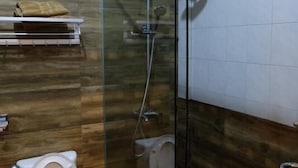 A bathroom with a glass-enclosed shower, a toilet, and a shelf with towels. - Holiday Hotel Batam (Batam)