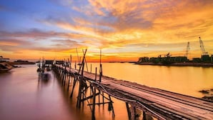 A wooden pier extending into calm water, with a sunset sky and distant industrial structures. - Holiday Hotel Batam (Batam)