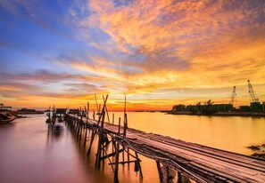 A wooden pier extending into calm water, with a sunset sky and distant industrial structures. - Holiday Hotel Batam (Batam)