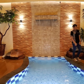 A man standing by a pool with a stone wall and two wall-mounted lights.