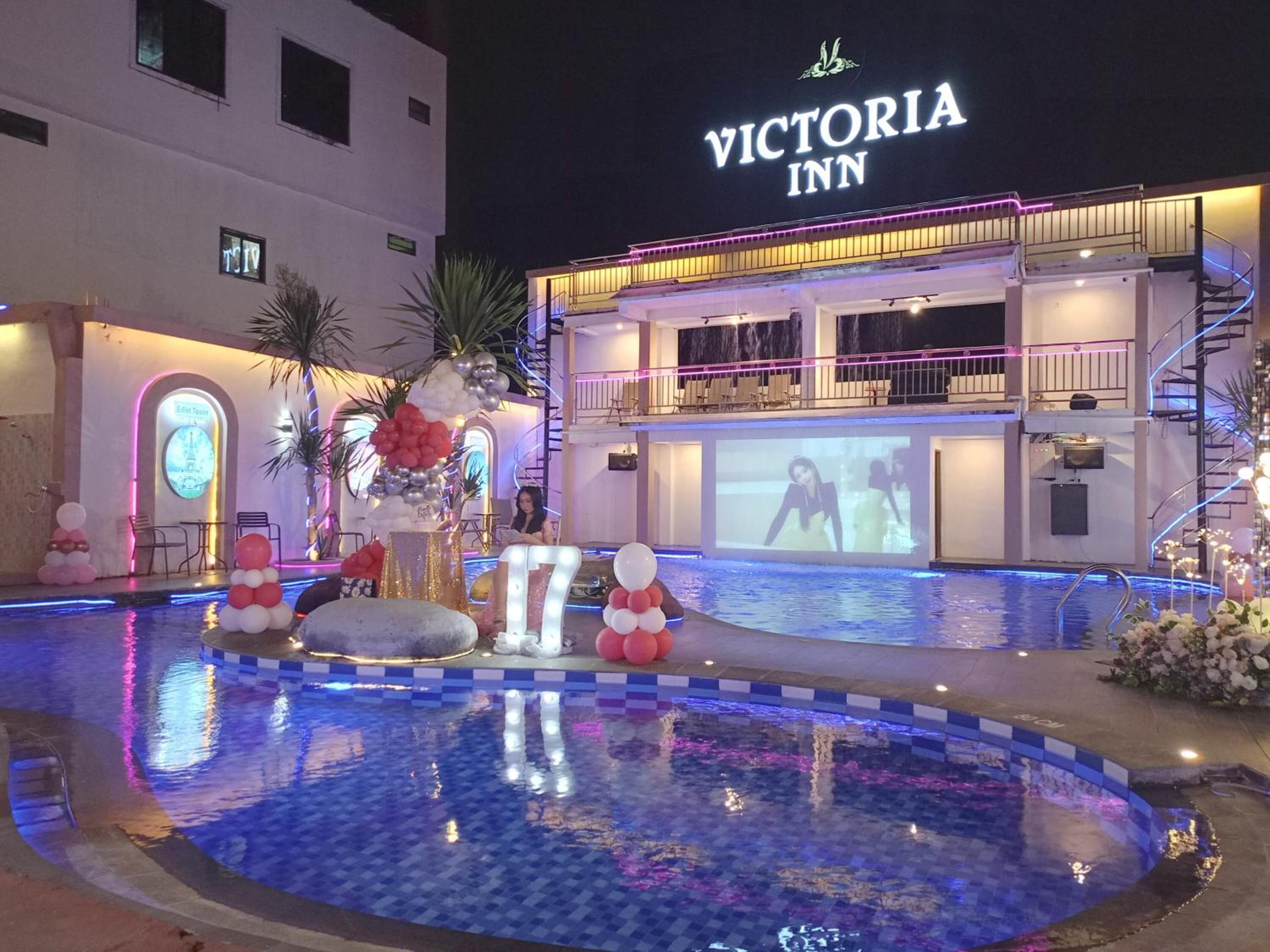 A pool area with a decorative setup and a building labeled "VICTORIA INN" in the background.
