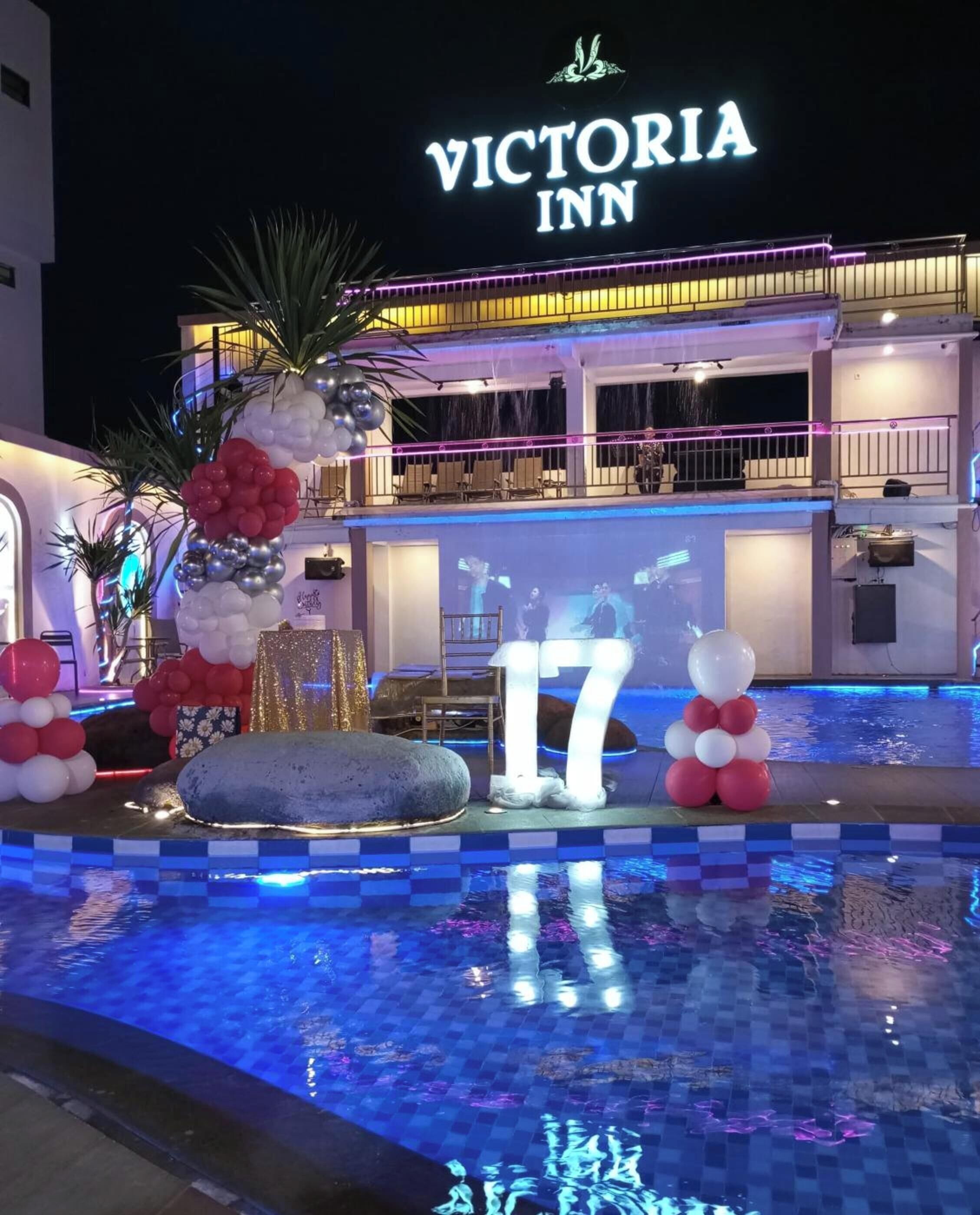 A pool area with a 'Victoria Inn' sign, a large '17' decoration, and a fountain.