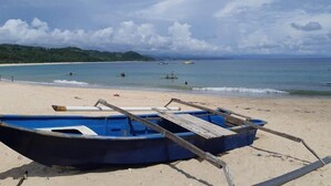 A beach with a blue boat on the sand, a clear sky, and calm sea.