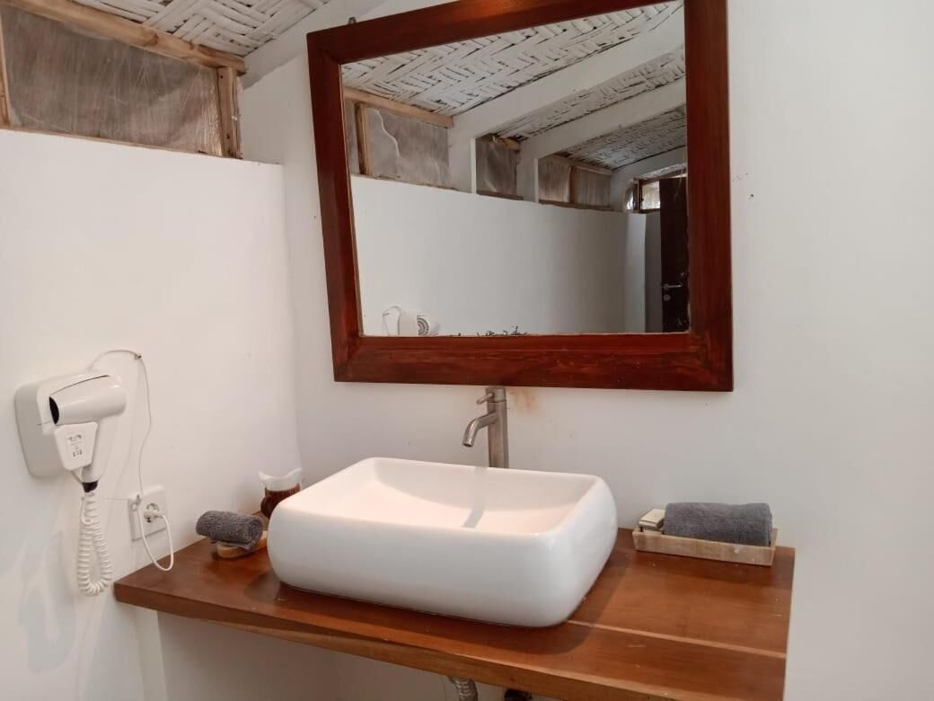 A bathroom with a white sink, a wooden vanity, a mirror, and a hairdryer on the wall.