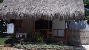 A thatched-roof hut with a simple, open porch and a small garden area in front.