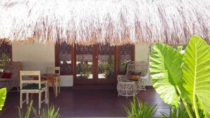 A covered outdoor seating area with thatched roof, wicker chairs, and large green plants.