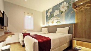 A hotel room with two beds, a large floral mural on the wall, a wooden headboard, and a small TV on the left. - Kaloka Airport Hotel (Sumbawa Besar)