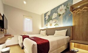 A hotel room with two beds, a large floral mural on the wall, a wooden headboard, and a small TV on the left. - Kaloka Airport Hotel (Sumbawa Besar)