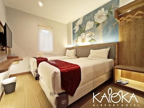 Een hotelkamer met twee bedden, een bureau, een televisie en een bloemstil afbeelding aan de muur.