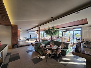 Een moderne loungehoek met een pooltafel, zitplaatsen en een groot raam met uitzicht op de omgeving.