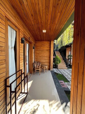 A wooden corridor with a wooden ceiling, a small table and chairs, and a staircase leading to an outdoor area with plants and a tiled path. - Sunrise Cottage Nusa Penida (Penida Island)
