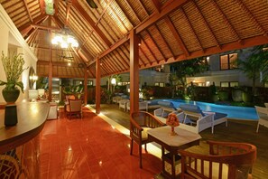 A covered outdoor area with a pool, lounge chairs, and a dining table.
