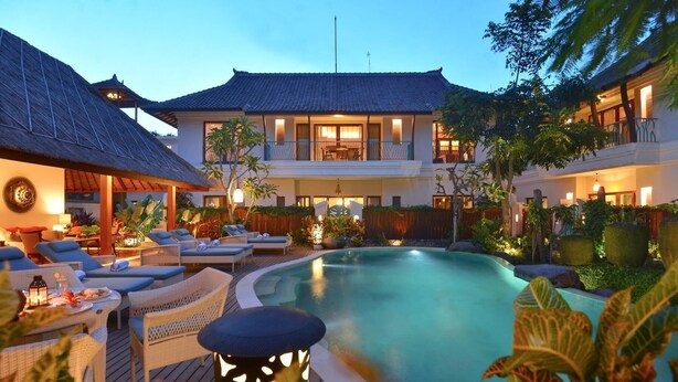 A resort with a swimming pool, lounge chairs, and a traditional building.