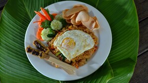 A plate of fried rice with a fried egg, vegetables, and skewers on a white plate.