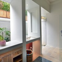 Un baño con un lavamanos blanco, un espejo, un mueble de madera y una planta en maceta.
